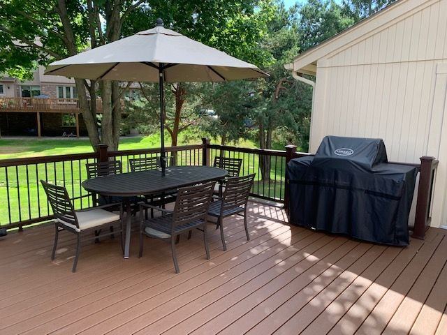 Sunny composite deck with black metal railings, a dining set under an umbrella and a covered grill