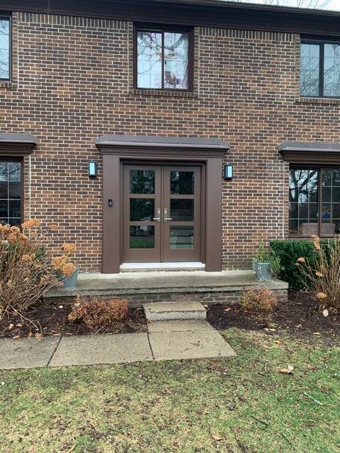 The same brick colonial with new brown double doors with glass upper lites under a pediment
