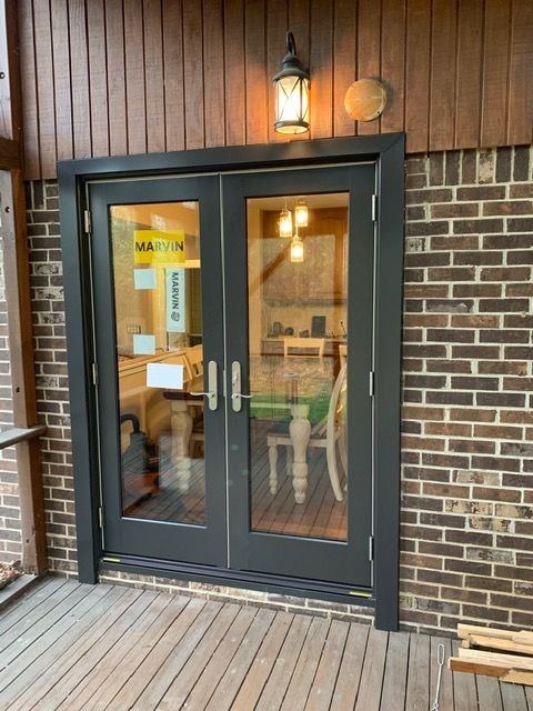 New black French doors with the manufacturer label still on the glass, opening onto a wood deck