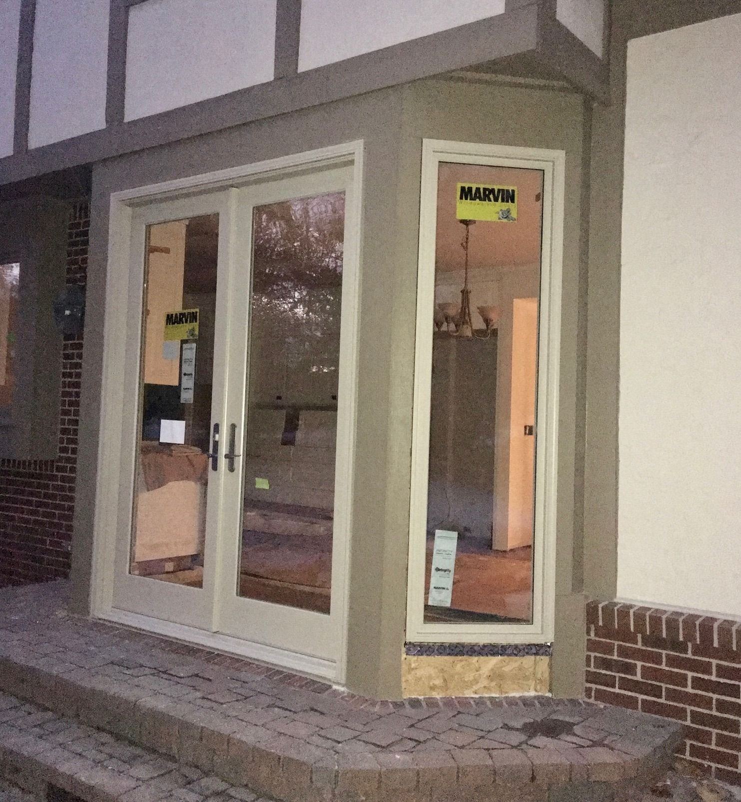 Tudor-style rear bay during install: new tan French doors and sidelight with labels still on the glass
