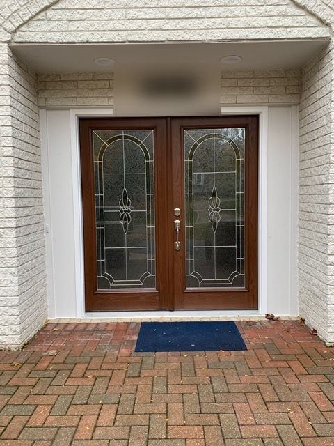 Close view of stained double entry doors with leaded glass over a herringbone brick stoop