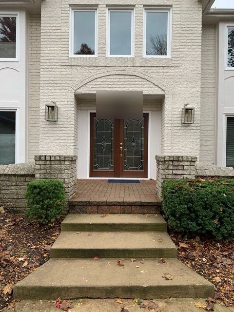 Stained double entry doors with leaded glass under an arched portico of a white brick home, wide stone steps