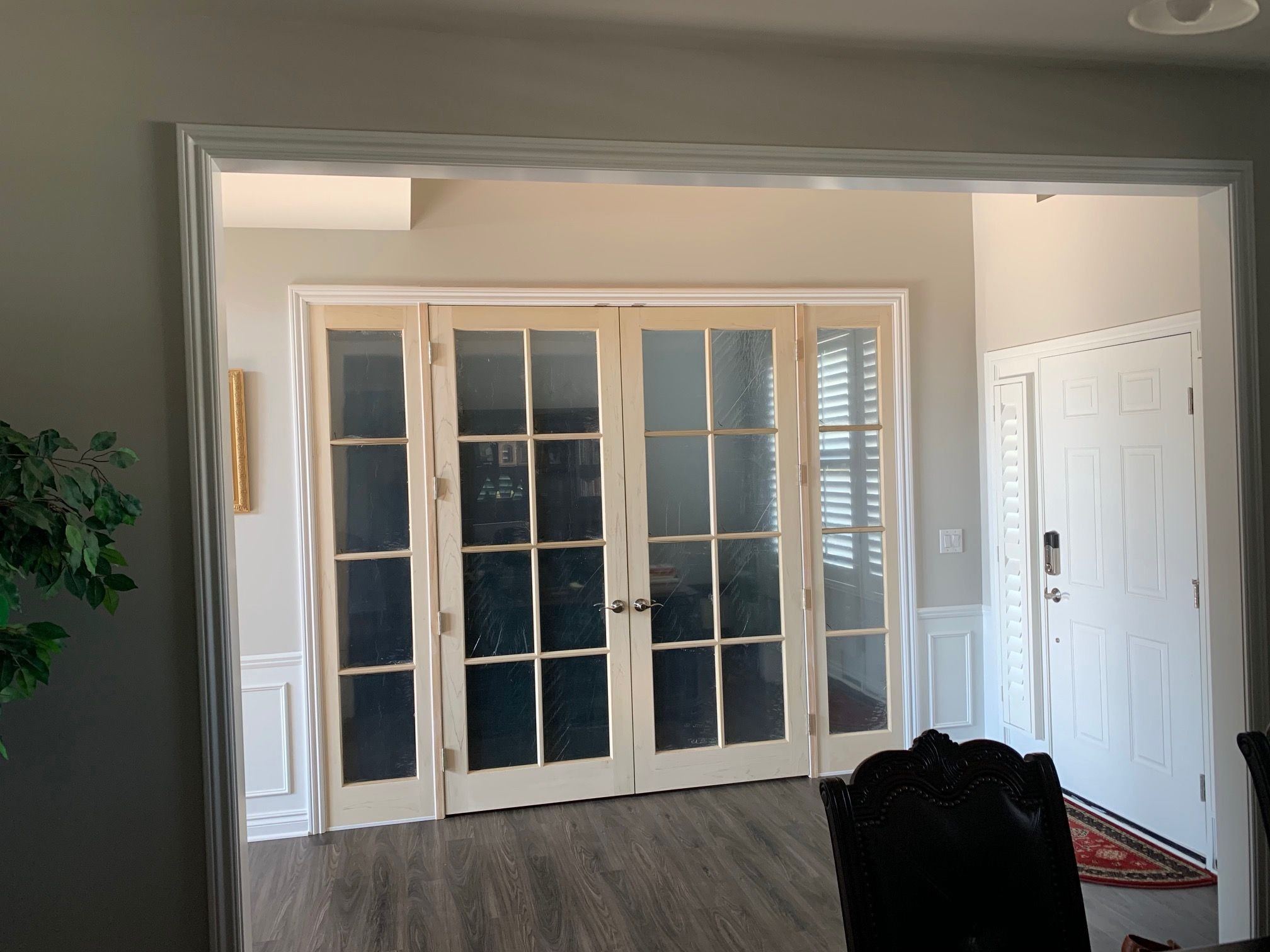 Wide white multi-lite interior French doors with matching side panels between a living room and a bright room