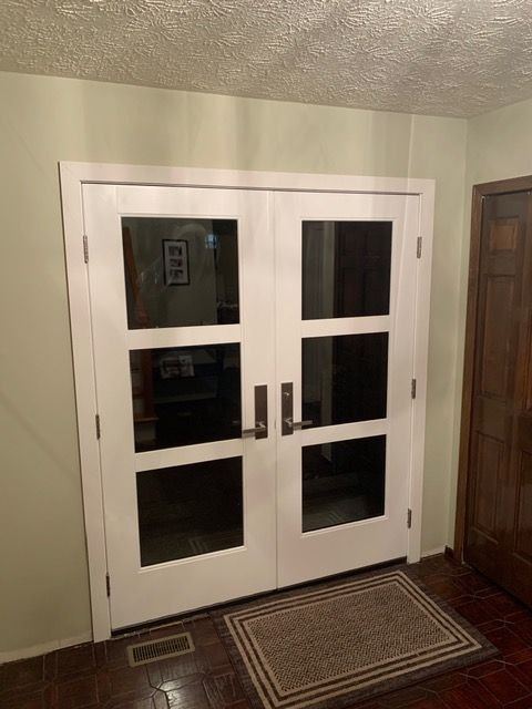White double front doors with three glass lites each, seen from a foyer with dark tile floor
