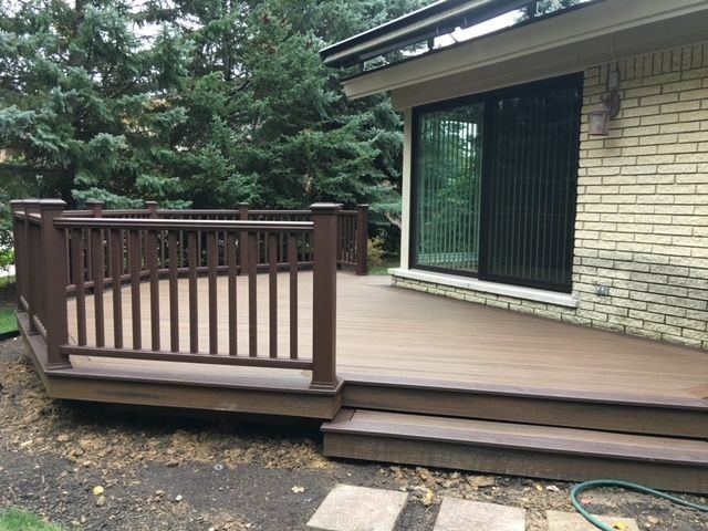 Low two-tone composite deck with brown railings and a wide step beside a light brick ranch