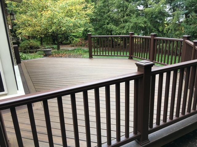 Brown composite railing posts and balusters wrapping a low deck, looking out to a tree-lined yard