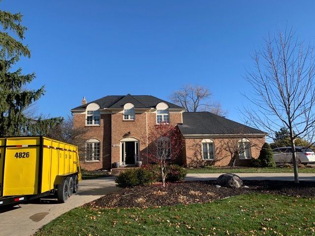 Front of a brick colonial with a new roof and a roll-off dumpster in the driveway