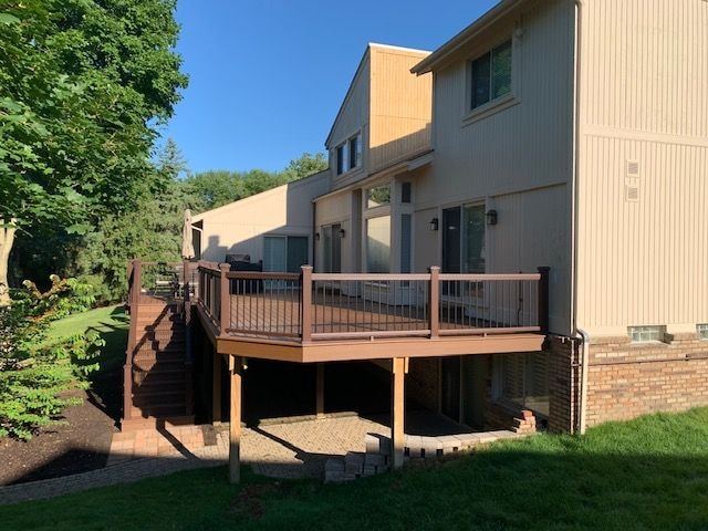 Raised composite deck with stairs on the back of a two-story tan home