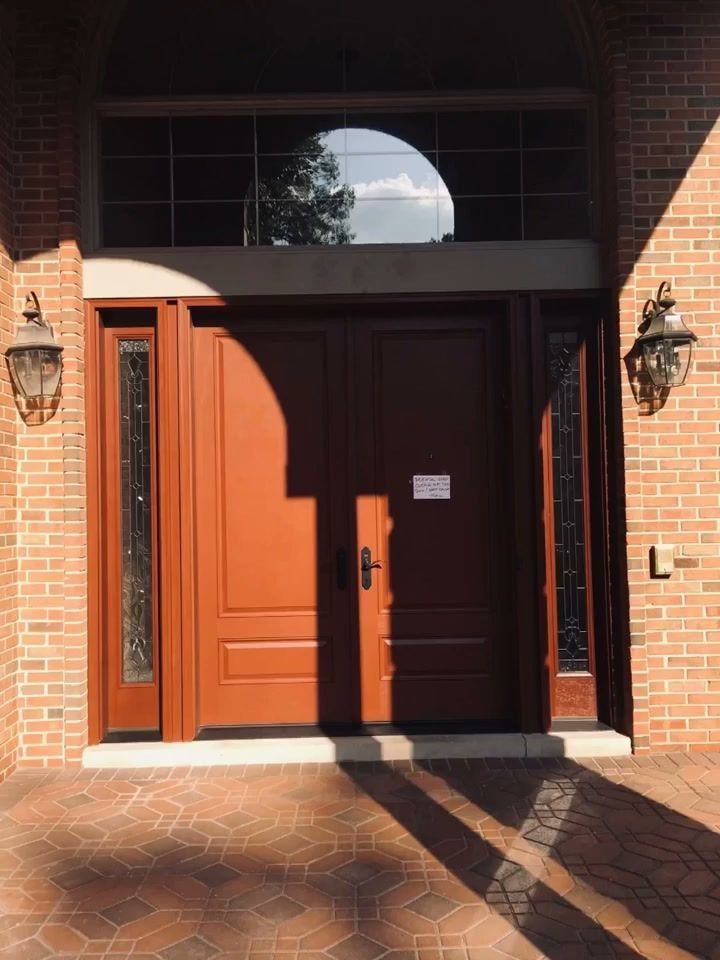 Stained double entry doors with leaded sidelights under an arched transom on a brick home, lit by late sun