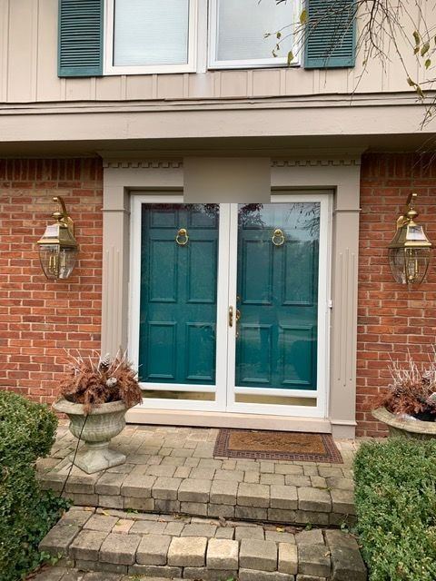 Teal double front doors behind new white full-view storm doors on a red brick home with brass lanterns