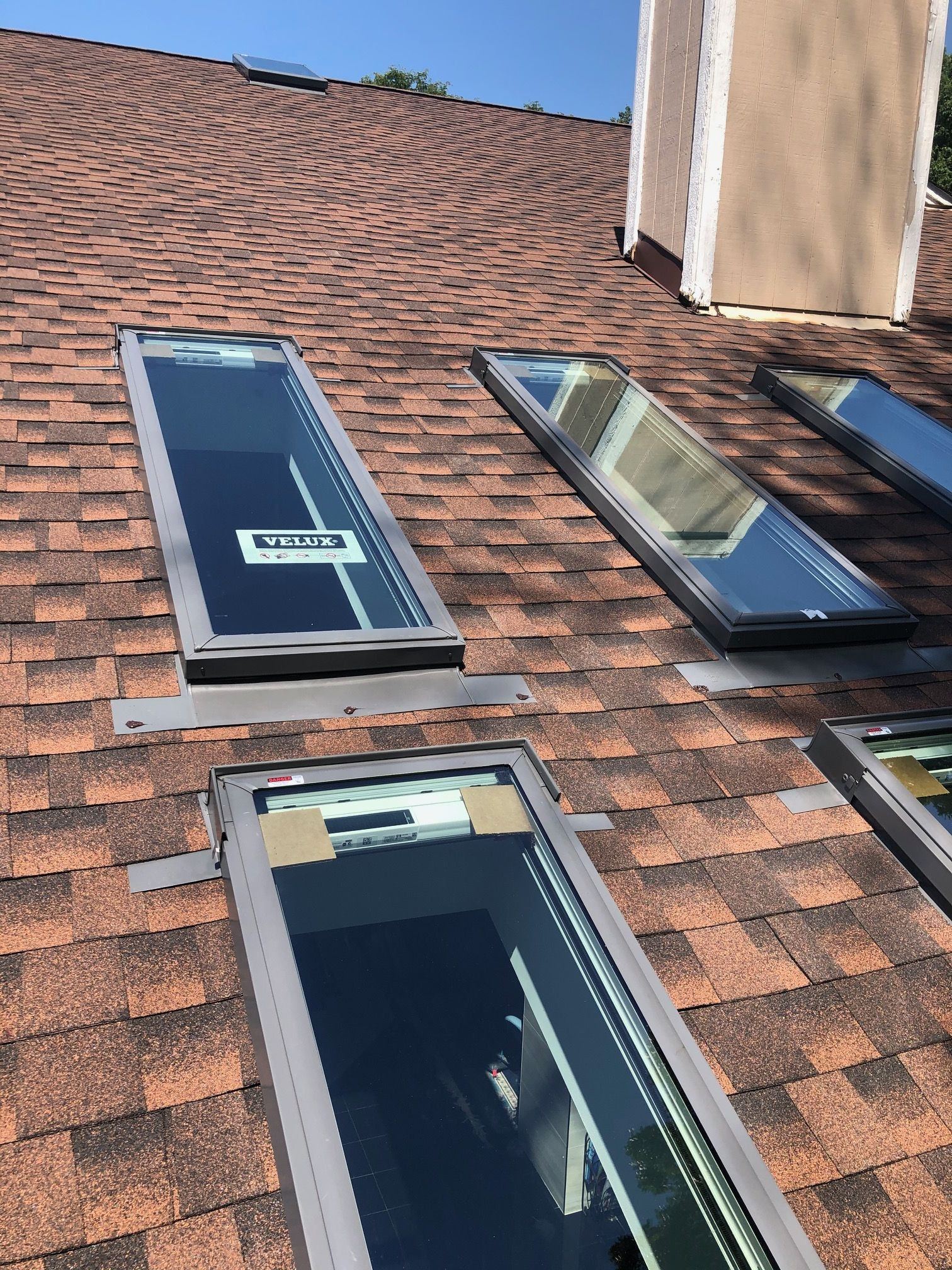 Close view of new VELUX skylights near a chimney on a reddish shingle roof